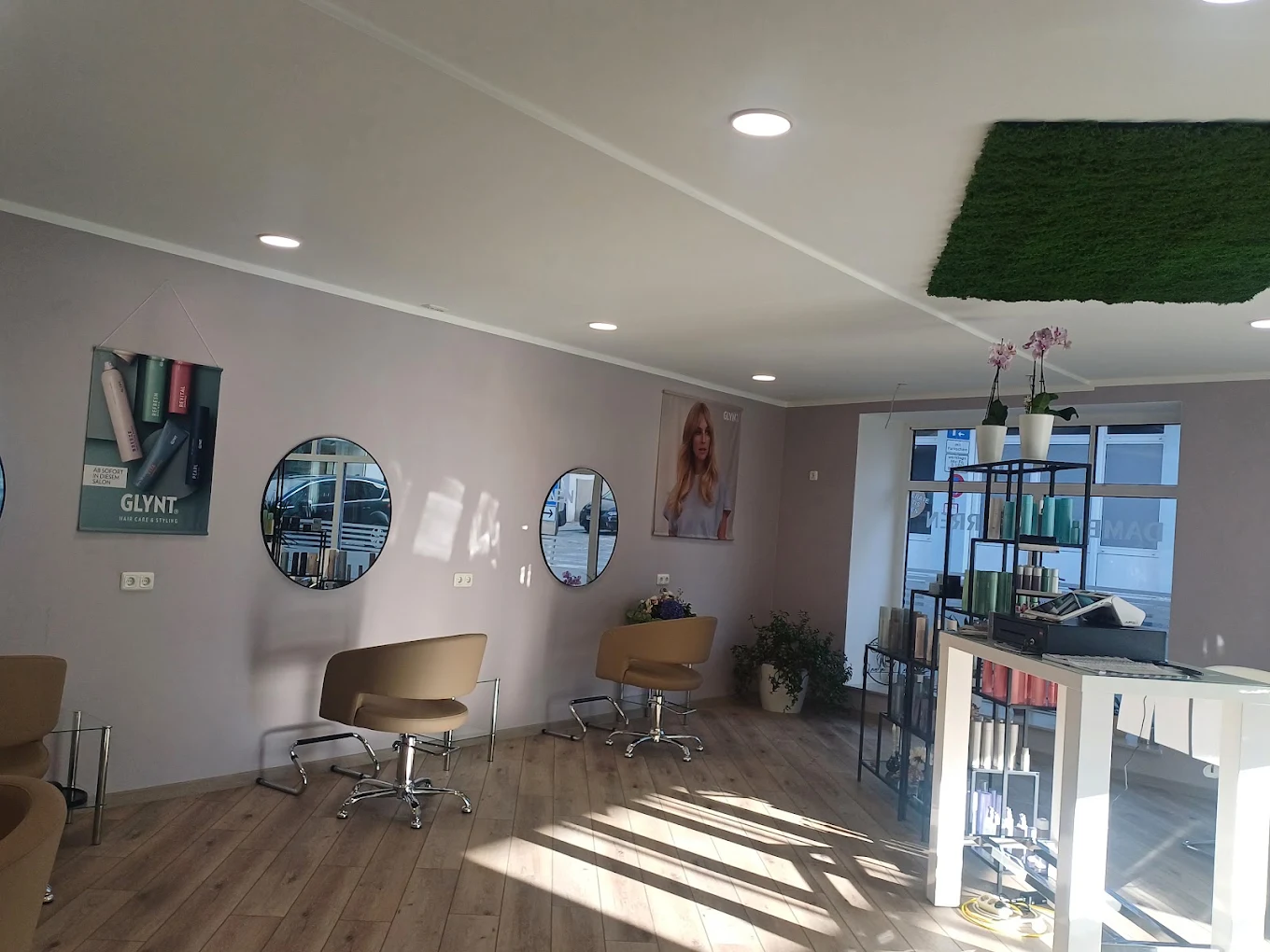 Friseurstühle vor runden Spiegeln an mauvefarbener Wand, Holzboden im Salon
